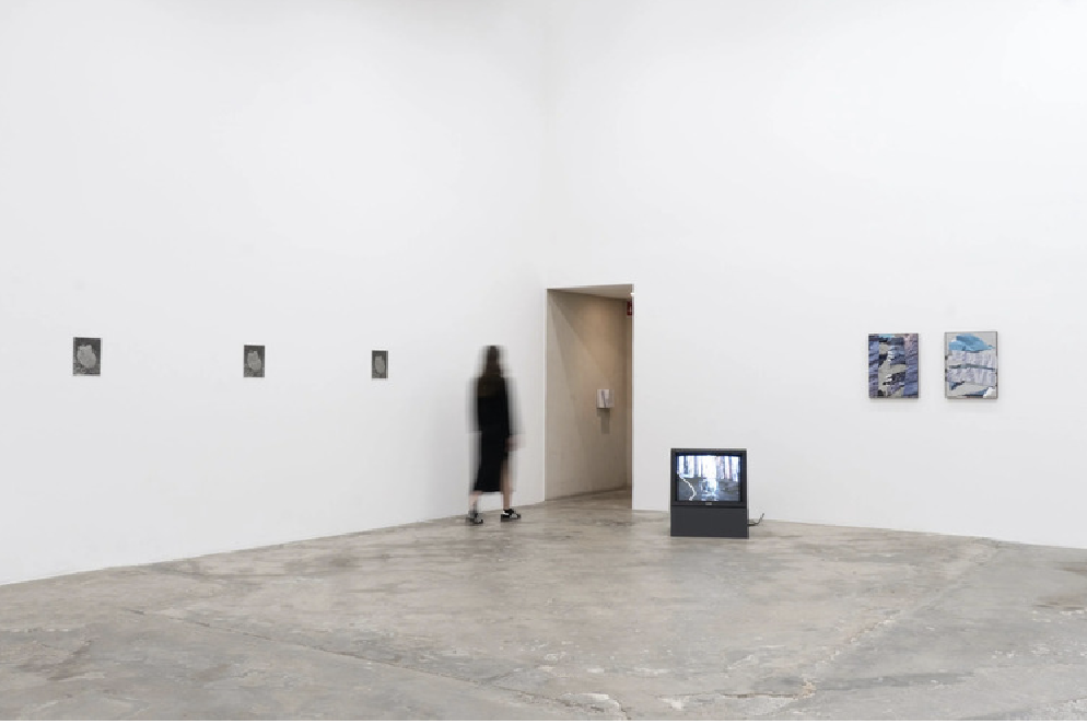 Sala blanca con un monitor, obras pequeñas en la pared y una persona frente a un umbral.