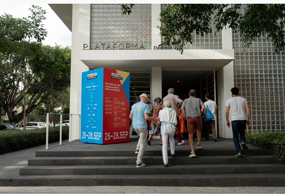 Visitantes suben las escaleras de un edificio blanco con el letrero Plataforma.